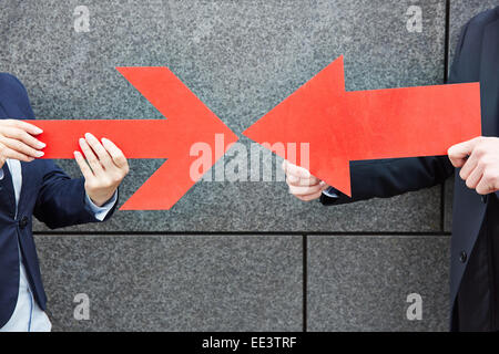 Due uomini di affari che dispositivo di puntamento con due grandi frecce rosse a ciascun altro Foto Stock
