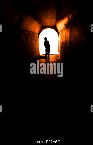 Persona in un tunnel lungo la passerella con luce bianca alla fine Foto Stock