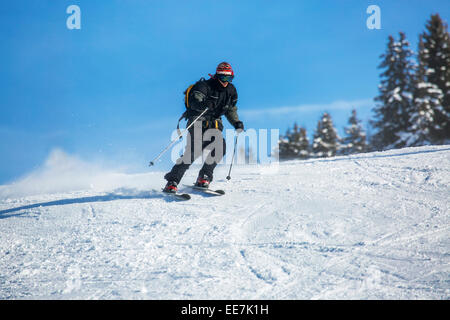 Sciatore uomo in abito da sci nero e occhiali da sci in discesa attraverso  neve in polvere profonda. Freerider giovane uomo in casco con bastoni da sci  e scivolando sulla neve presso