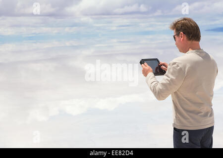 Uomo al lavoro su tavoletta digitale nel mezzo del lago Salar de Uyuini, Bolivia Foto Stock