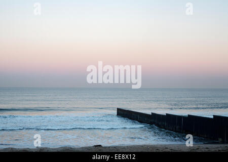 Sunrise a Tijuana beach in Messico, mostrando la USA - confine messicano recinzione in esecuzione nell'Oceano Pacifico. Foto Stock