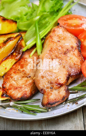 Bistecche di carne arrosto con patate al forno e verdure fresche sul tavolo rustico Foto Stock