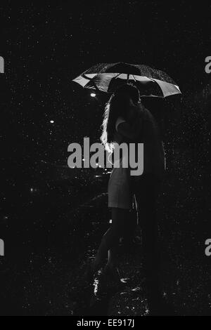 L'amore sotto la pioggia / Silhouette di baciare giovane sotto ombrellone Foto Stock