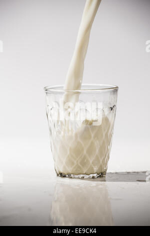 Versare il latte in un bicchiere isolata contro uno sfondo bianco Foto Stock