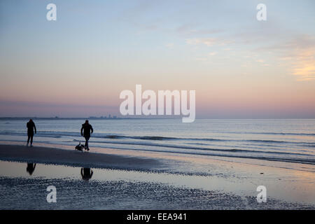 Persone e cane sulla spiaggia al tramonto sul Mare del Nord costo dei Paesi Bassi con silhouette di Zandvoort in background Foto Stock