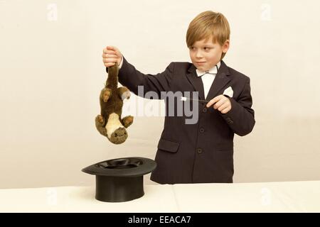 Ragazzo giovane vestito come un mago tira un giocattolo morbido dal suo top hat Foto Stock