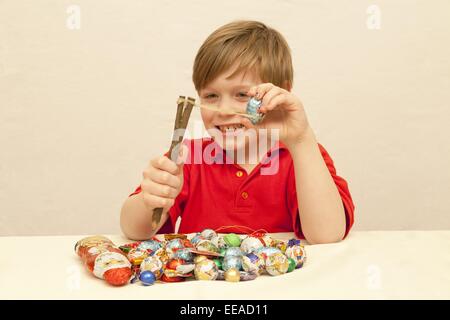 Ragazzo con un mucchio di dolci di Natale di fronte a lui i dolci di scatto con una fionda Foto Stock