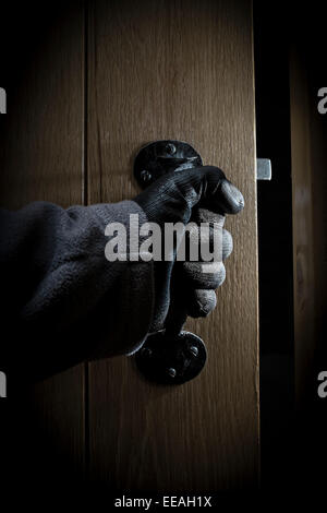 La mano guantata aprendo una porta in una stanza buia. Foto Stock