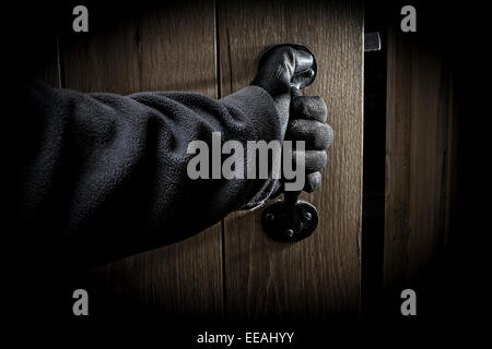 La mano guantata aprendo una porta in una stanza buia. Foto Stock