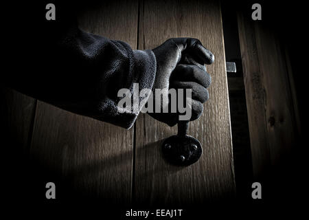 La mano guantata aprendo una porta in una stanza buia. Foto Stock