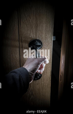 Una mano d'uomo l'apertura di una porta in una stanza buia. Foto Stock