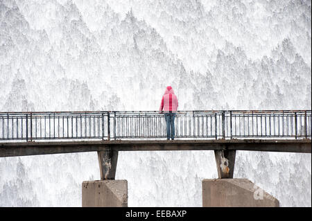 Acqua a cascata verso il basso serbatoio scarico di troppo pieno, con la persona che osserva da un ponte. Foto Stock