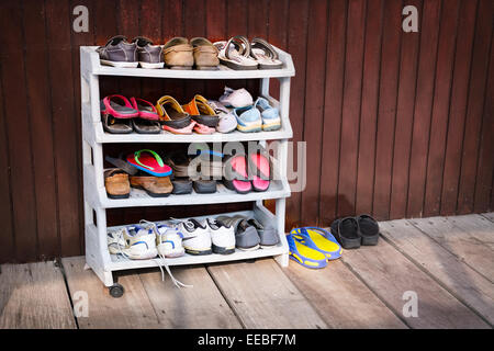 Una varietà di scarpe colorate, perfettamente ordinato su un pattino di plastica cremagliera al di fuori di una casa in legno. Foto Stock