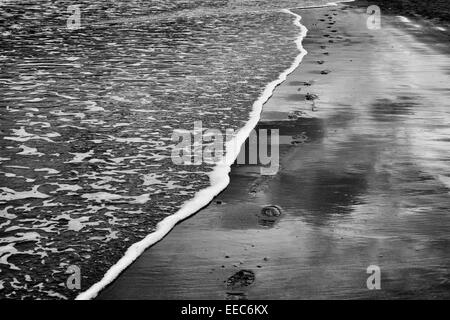 Orme nella sabbia vicino al mare con la bassa marea. Regno Unito. In bianco e nero Foto Stock