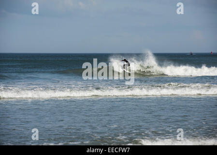 Una solitaria giovane uomo in nero di una muta umida è indietro di taglio su un'onda come egli surf litorale orientale della Florida vicino a Daytona Beach. Foto Stock