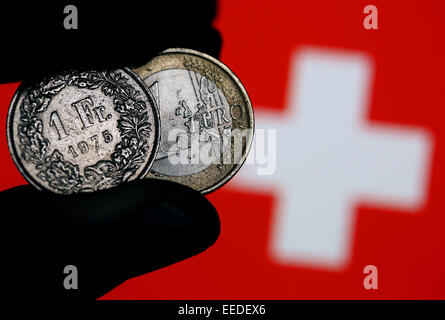 Un Euro moneta (L) e un franco svizzero sono in esposizione su un cittadino svizzero bandiera a Colonia, Germania, 15 gennaio 2015. Il disaccoppiamento del franco svizzero dall'Euro ha innescato le turbolenze sui mercati finanziari. Foto: Oliver Berg/dpa Foto Stock