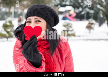 Capelli neri donne turche tenendo un cuore rosso con il nero caldo guanti di lana e di celebrare il giorno di San Valentino con sfondo innevato Foto Stock