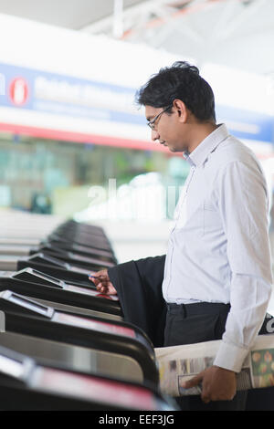 Asian commerciante indiano all'entrata della stazione ferroviaria, toccando il token del biglietto sulla barriera di gate. Foto Stock