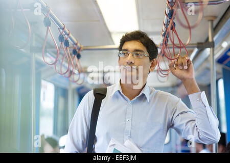 Asian Indian business man tenendo giro a lavorare, in piedi all'interno del treno. Foto Stock
