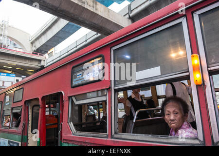 Anziana donna locale guarda fuori del bus locale finestra vicino a Siam Square,Bangkok, Tailandia,Asia.Traffico,auto,scooter,autobus,Sky Train Foto Stock