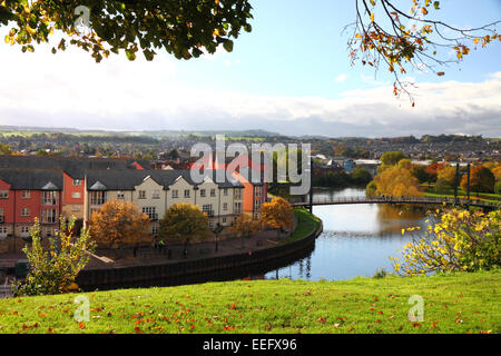 Una vista di un fiume calmo con una moderna passerella, case e fogliame di autunno. Foto Stock
