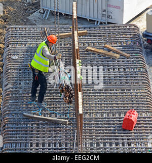 Steelfixer guidare una gru bundle di abbassamento dei tondini di acciaio sul telaio di fondazione sito in costruzione Londra Inghilterra REGNO UNITO Foto Stock