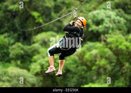 Oversized donna adulta su Zip Line viaggio messa a fuoco selettiva contro sfocata foresta di pioggia Foto Stock