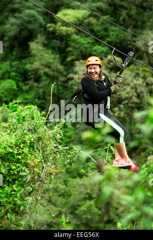 Oversized donna adulta su Zip Line viaggio messa a fuoco selettiva contro sfocata foresta di pioggia Foto Stock