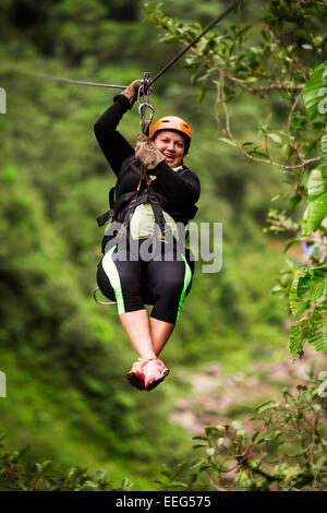 Oversized donna adulta su Zip Line viaggio messa a fuoco selettiva contro sfocata foresta di pioggia Foto Stock