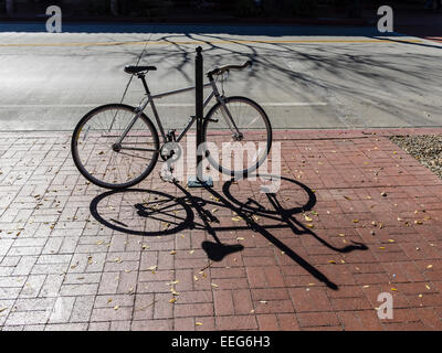 Una due ruote di bicicletta è parcheggiata e agganciato ad un palo su un marciapiede di mattoni su State Street a Santa Barbara, California. Foto Stock