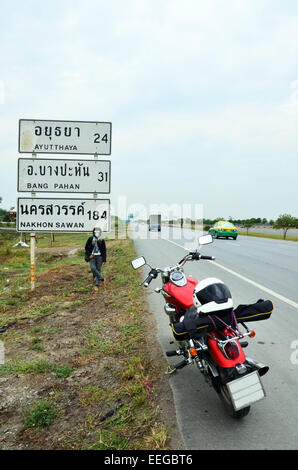 Donna tailandese di equitazione motocicletta del trinciapaglia sul modo in cui andare a Ayutthaya con guidepost o segni di distanza Foto Stock