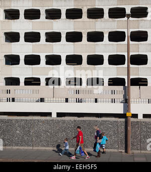 Gruppo di famiglia a piedi passato brutto parcheggio multipiano (rampa) a Worthing West Sussex, in Inghilterra. Foto Stock