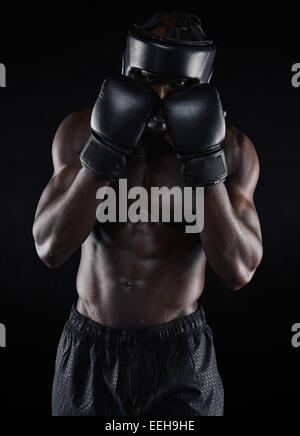 Ritratto di un giovane maschio boxer in un atteggiamento di combattimento su sfondo nero. Africa boxer maschio bloccando il suo volto con i guanti. Foto Stock