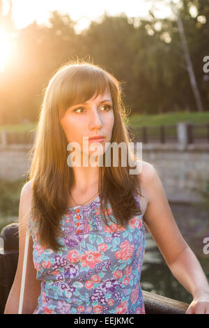 I giovani adulti ragazza sogna nella luce del tramonto. La donna caucasica in attesa che qualcuno alla sera d'estate Foto Stock