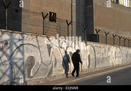 Uomo che cammina lungo la strada passato coperto di graffiti di muro di fabbrica in urban area industriale, vicino a Badalona, Barcellona Foto Stock