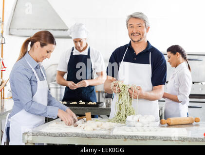 Sorridente chef maschio con i colleghi di preparare la pasta in cucina Foto Stock