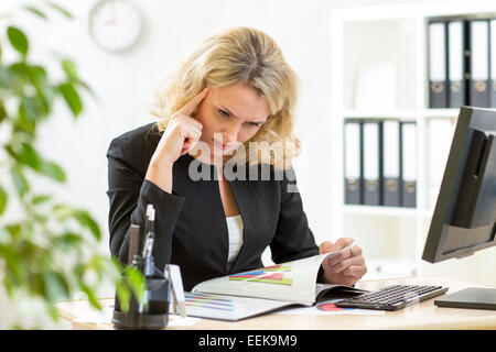 Di mezza età business donna che lavorano in ufficio e esaminando i rapporti Foto Stock