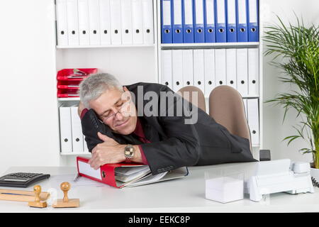 Mann mittleren altera sitzt im Büro, liegt auf Akternordnern und schläft, uomo di mezza età, seduto nel suo ufficio, giacente su offic Foto Stock