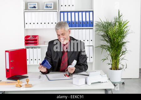 Mann mittleren altera sitzt im Büro am Schreibtisch mit leerer Tasse Kaffee in der mano, uomo di mezza età si siede in un ufficio Foto Stock