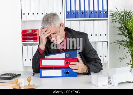 Mann mittleren altera sitzt im Büro, hält sich den Kopf, hat Kopfschmerzen, uomo di mezza età con un mal di testa, si siede nel suo ufficio, Foto Stock