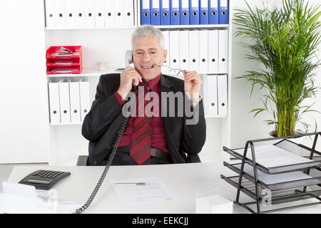Mann mittleren altera sitzt im Büro und telefoniert, uomo di mezza età seduto nel suo ufficio, telefonare Foto Stock
