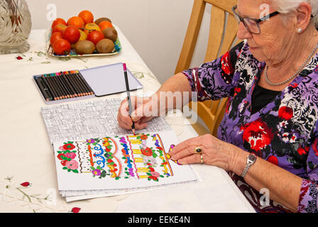 Donna anziana occupato con matite colorate in un libro da colorare Foto Stock