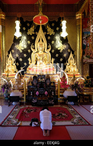 Un pellegrino buddista pregando Buddha figura all'interno della pagoda di Wat Neramit Wipattasana tempio che è famosa per le sue grandi dimensioni ordinazione hall e la pagoda costruita di colore rosso laterite nella provincia settentrionale di Loei in Thailandia Foto Stock