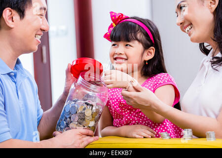 Famiglia cinese di risparmio di denaro per college fund del bambino, mettendo le monete in vaso Foto Stock