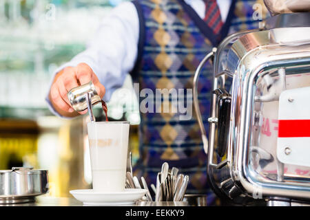 Barista in bar o caffè bar preparare versando colpo espresso in un bicchiere di latte macchiato Foto Stock