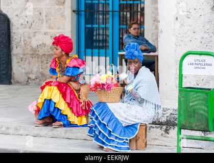 Vista delle donne locali vestiti in colorati abiti tradizionali per i suggerimenti che vendono fiori in piazza Duomo, Old Havana, Cuba, rossetto Foto Stock