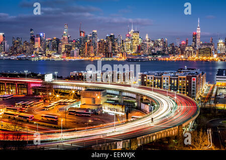 Traffico e sentieri di luce sull'elica di una autostrada loop all'ingresso in Lincoln Tunnel. Lo skyline di New York risplende nella parte posteriore Foto Stock