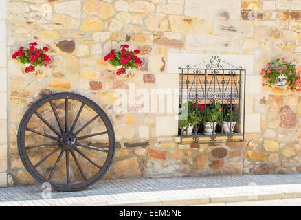 Finestra rustico di una casa contadina decorate con vasi di fiori e di legno ruota del carro Foto Stock