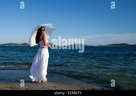 Donna sorridente in piedi vicino al mare che tiene un ombrellone, Grecia Foto Stock