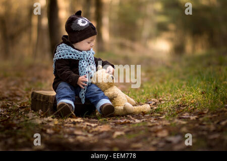 Ritratto di bambino seduto nella foresta con il suo orsacchiotto di peluche Foto Stock